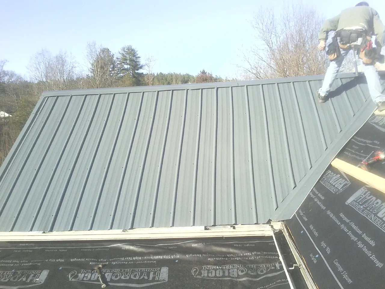 Crew installing dark green standing seam panels over synthetic underlayment in Roxbury