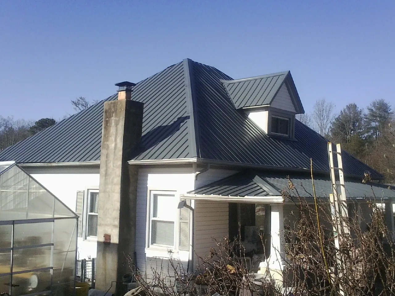 Dark blue standing seam metal roof on a white farmhouse with dormer — Slate & Tile Roof Repair by Roofing Brothers in Roxbury