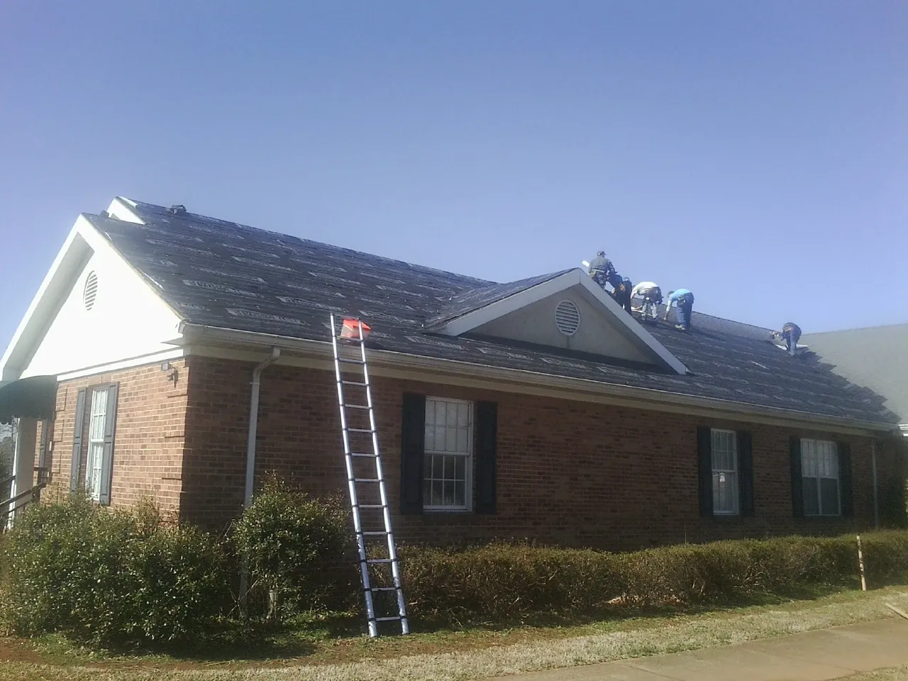 Crew tearing shingles off a brick ranch roof with a ladder set — Emergency Roof Repair work by our crew in Roxbury