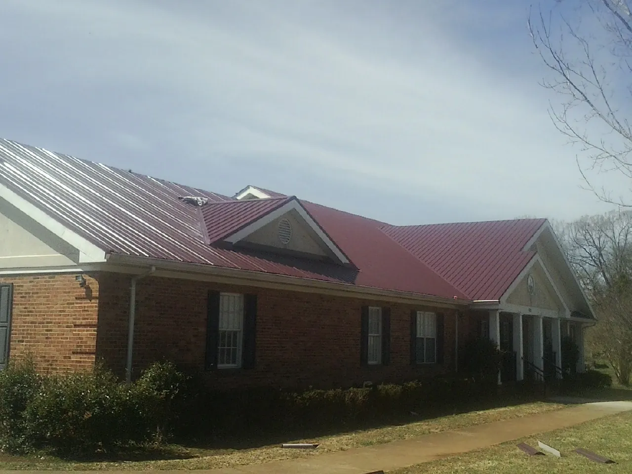 Red metal roof with gabled entries on a long brick building, from a Hail Damage Roof Repair job in Roxbury